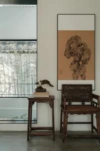 A modern living room featuring wooden furniture and stone accents, with a bonsai tree on a small wooden table and a framed ar