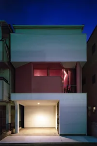 A modern residential building with a minimalist design, featuring concrete exterior and a glowing interior.