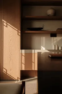 A minimalist modern kitchen with wooden cabinets and shelves, featuring a countertop with a marble or similar stone finish.