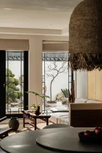 A minimalist living room with neutral-colored walls and furniture, featuring a large window with a view of a garden.