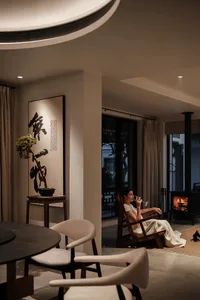 簡約住宅室內，一名女子慵懶地躺在壁爐旁，旁邊有圓形餐桌與裝飾用盆栽