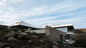 A modern house with a concrete structure and large windows overlooking the landscape.