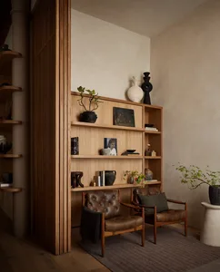 A modern living room featuring wooden shelves, leather armchairs, and decorative items.