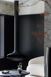 A minimalist living room with a black steel fireplace and white armchair, featuring sleek and modern design elements.