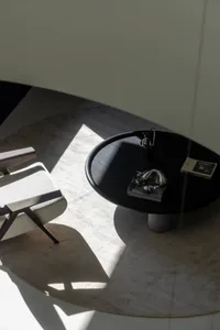 A modern living space featuring a sleek black coffee table with glass legs and marble top placed on a textured rug.