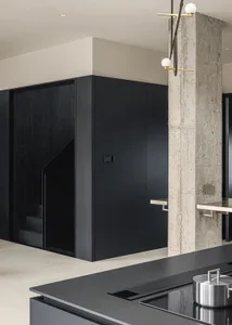 A modern kitchen with black wooden cabinetry and a concrete wall.