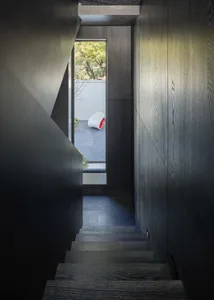 Modern interior featuring black wooden stairs and a minimalist aesthetic, with a white chair with a red bottom visible throug