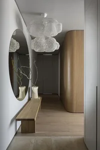 Modern minimalistic entryway with large wooden bench, circular mirrors, and glass chandelier with floral design.