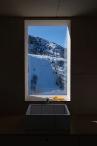 Modern bathroom with a concrete sink, yellow soap dish, white toothbrush, and a window overlooking a snow-covered mountain la