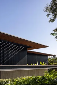 Modern black metal-clad building exterior with large overhang and green foliage.