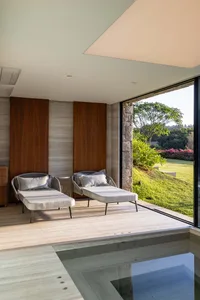 Contemporary living room featuring modern furniture, wooden walls, stone accents, and large glass windows overlooking a lush 