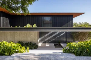 A modern house with a metal-clad exterior featuring a large window and greenery.