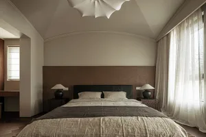 Modern minimalist bedroom with textured wallpaper, large bed, two side tables, lamps, and a window with sheer curtains.