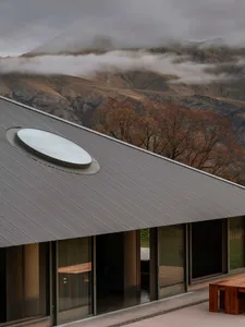 Modern residential house with a metal roof and large windows overlooking a mountainous landscape.