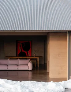 A modern living room with a pink fabric sofa, concrete walls, and a corrugated metal roof.
