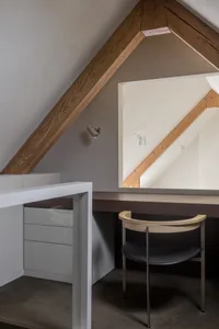 A modern home office features a concrete floor, wooden beams, and a metal desk.