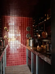 An industrial-style kitchen with red tile walls, metallic appliances, and various cooking utensils.