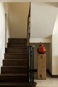 A modern staircase with wooden steps and handrail, featuring a red pear-shaped object on a wooden pedestal.