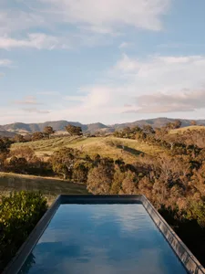 A tranquil poolside view overlooking green rolling hills and scattered trees under a partly cloudy sky.