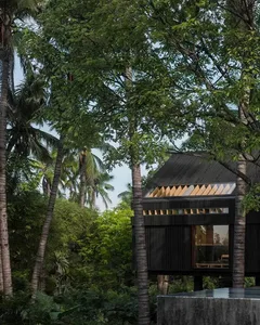 Modern minimalist treehouse with wooden exterior, glass windows, and concrete foundation.
