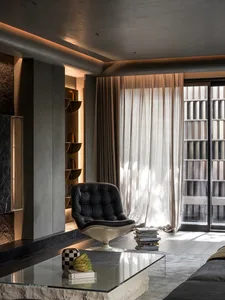 A modern interior design featuring a sleek black leather chair, a glass coffee table, concrete walls, and glass doors with su
