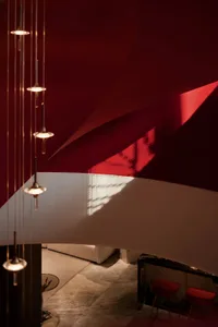 Red fabric wall and ceiling with hanging lights and a view of a seating area with a white sofa and red stools.