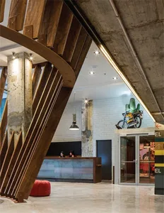 Modern industrial-style lobby featuring exposed concrete walls and wooden beams, with a reception desk and seating area.