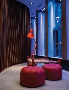 Modern minimalist interior space featuring a red floor lamp, wooden seating, and a red pouf.