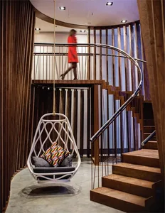 A modern living space featuring a suspended white chair with colorful cushions and wooden stairs.