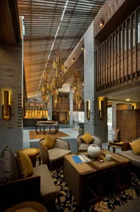 Spacious hotel lobby with wooden floors and furnishings, featuring tall ceilings with wooden slat ceiling and hanging chandel