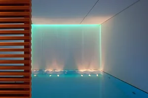 A modern minimalist swimming pool with a glass wall and ambient lighting.