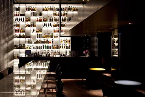 A modern bar with backlit metallic shelves displaying a variety of bottles and a sleek, contemporary design.