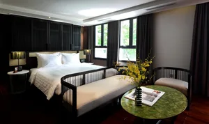 A modern minimalist bedroom with a queen-sized bed, wooden furniture, and large windows letting in natural light.