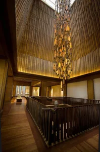 A minimalist wooden interior with a high ceiling, wooden beams, and a large chandelier hanging from the ceiling.