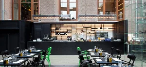 A modern restaurant interior featuring black and green accents, with a bar, tables, chairs, and a glass display case.