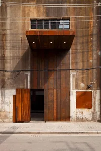 A rustic steel building exterior with a large wooden door and a small window above it.