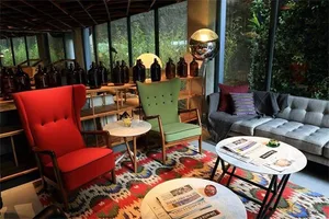 A cozy industrial-style coffee shop interior with various seating options, decorative lighting, and a view of greenery outsid