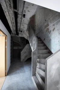 An industrial-style concrete staircase leading upward with exposed pipes on the ceiling.