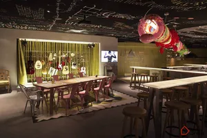 Industrial-style restaurant and bar interior with metal tables, wooden chairs, and glass chandeliers.