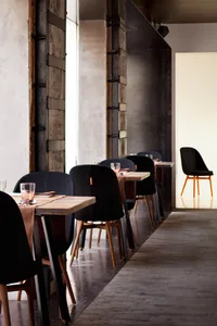 Industrial-style restaurant interior with wooden tables, concrete walls, and black chairs and accents.