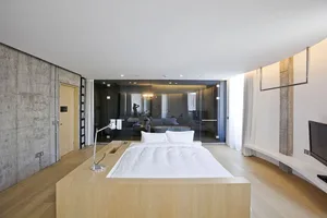 Modern minimalistic bedroom featuring a wooden floating platform bed, white bedding, and minimalist decor.