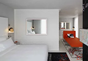 A minimalist hotel room featuring a white brick wall, concrete floor, and a red lounge chair.