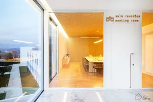 Modern conference room with white marble floor and wooden walls. A large glass wall provides a view of the outdoor area.
