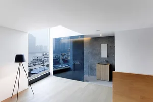 A modern living room with a waterfront view, featuring concrete and glass materials.