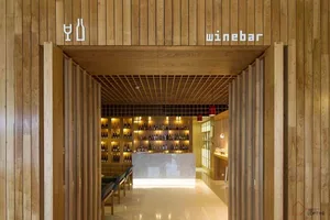 Modern minimalist bar interior with wooden walls and shelves filled with bottles.