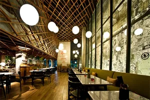 A spacious modern restaurant with industrial design elements including wooden beams, concrete walls, and large glass windows.