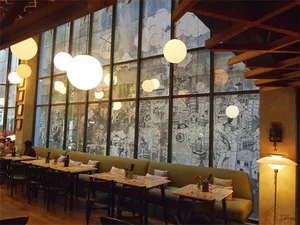 Modern restaurant interior with large windows, bench seating, and hanging spherical lights.