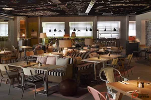 A modern restaurant interior with metallic furniture and colorful cushions, featuring large windows and a black ceiling with 