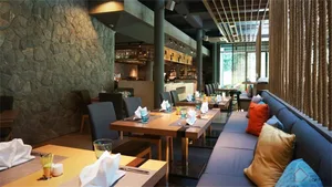 Modern restaurant interior with stone wall, wooden tables, and blue seating area.