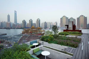 Urban rooftop garden with concrete planters and seating areas overlooking a city skyline.